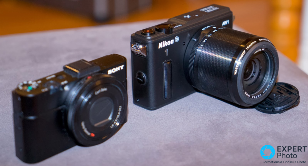 Nikon 1 AW1 noir et hybride Sony noir posés côte à côte sur surface grise, comparaison de gabarit