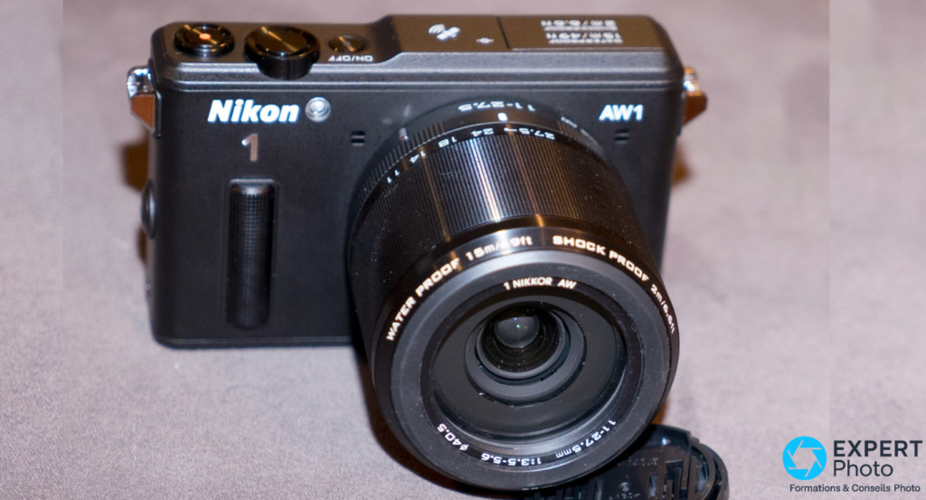  Nikon 1 AW1 noir, vue 3/4 avant, objectif 1 Nikkor AW 11-27,5 mm f/3,5-5,6 monté, fond gris uni