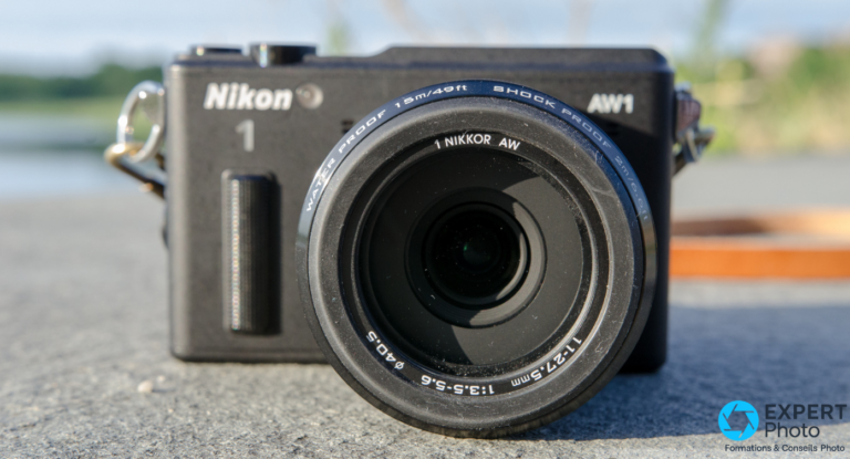 Nikon 1 AW1 vu de face, objectif 1 Nikkor AW 11-27,5 mm f/3,5-5,6 ø40,5 marqué WATER PROOF 15m, fond flou