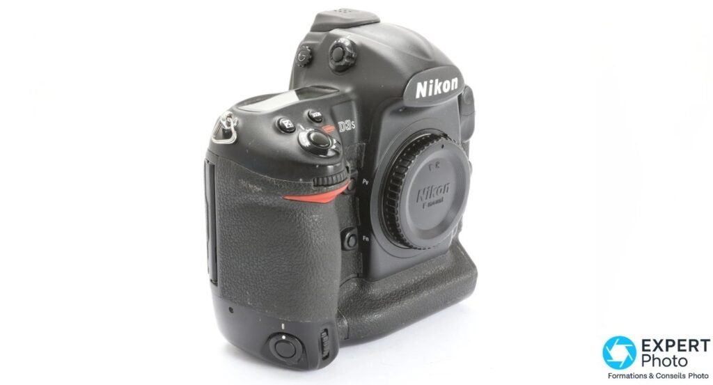 Nikon D3s vu de 3/4 avant gauche, monture F mount sans objectif avec bouchon, grip vertical integre et gravure D3s. 