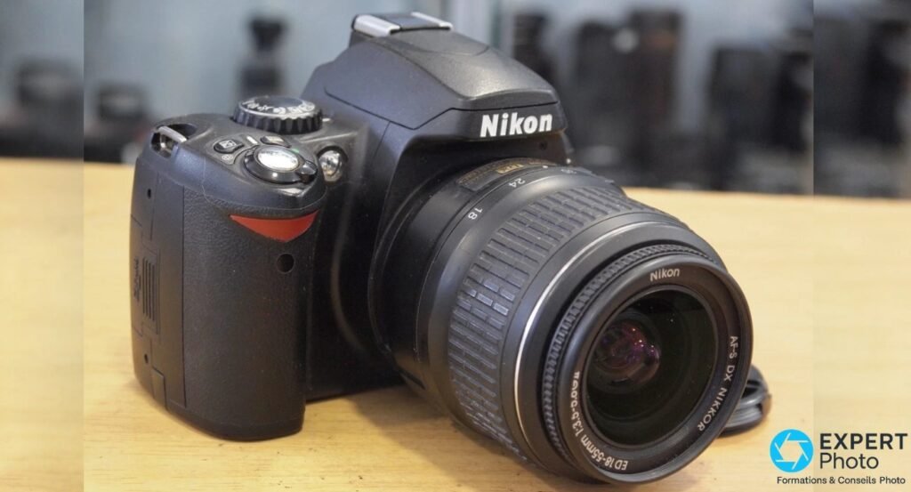 Nikon D40 en trois-quarts avant gauche avec objectif AF-S DX Nikkor 18-55mm zoom sorti, bouchon posé. 
