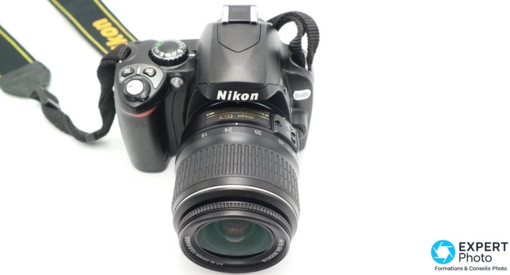 Nikon D40X vu en plongée 3/4 avant avec son objectif kit 18-55mm Nikon DX et la sangle Nikon en arrière-plan.