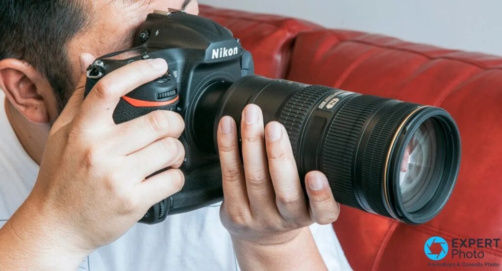 Photographe visant avec un Nikon D5 équipé d'un téléobjectif zoom Nikon en monture F, vue de profil trois-quarts gauche.