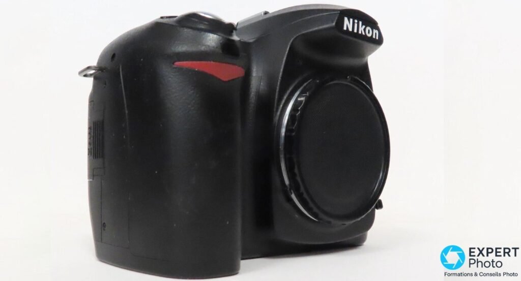 Reflex Nikon D50 noir vu de trois quarts avant gauche, cache de monture, grip avec liseré rouge en relief.
