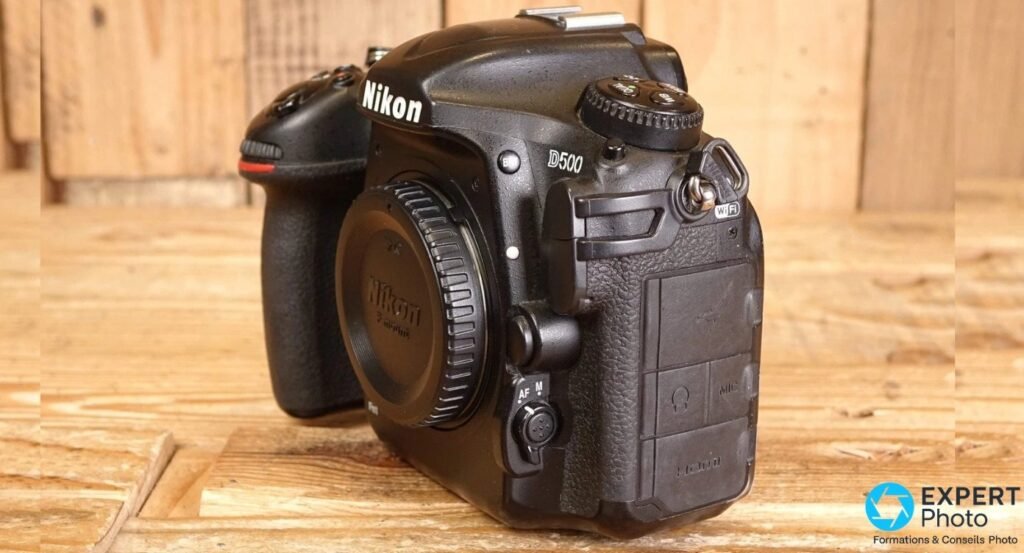 Face avant 3/4 d'un Nikon D500 noir avec marquages Nikon D500, Wi-Fi, sélecteur AF/M et trappe connectiques.