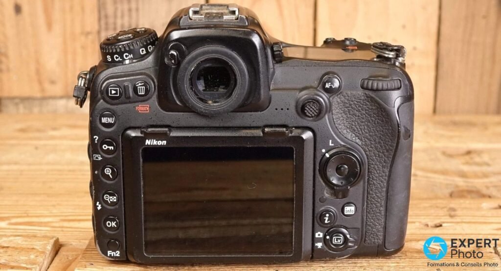 Dos plat d'un Nikon D500 montrant l'écran LCD, le pad directionnel, la molette drive S/CL/CH/Q et les commandes de gauche.