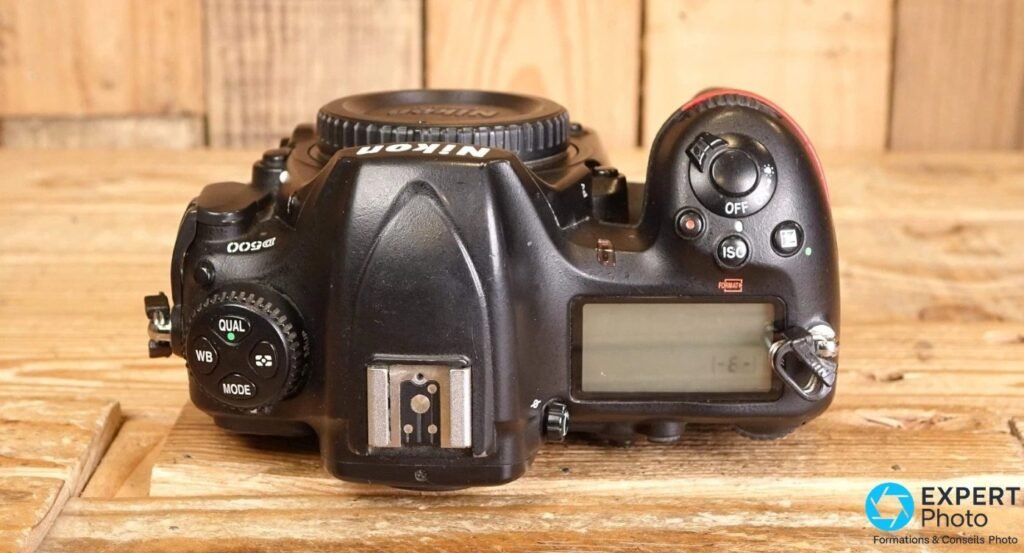 Dessus d'un Nikon D500 montrant l'écran LCD secondaire, la molette QUAL/WB/MODE et la griffe porte-flash.