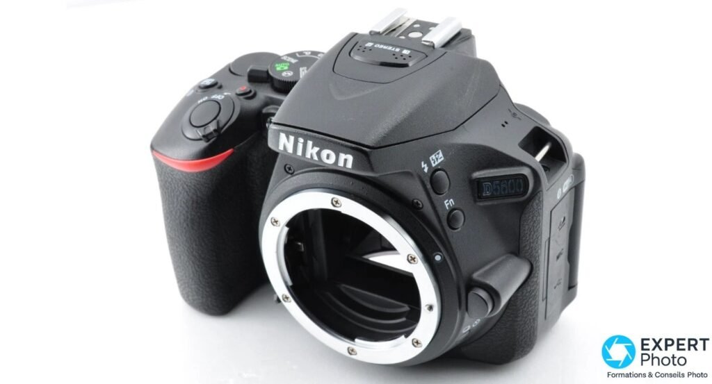 
Boîtier Nikon D5600 nu en 3/4 avant droite, monture Nikon F sans objectif, logos Nikon et D5600 visibles, fond clair.