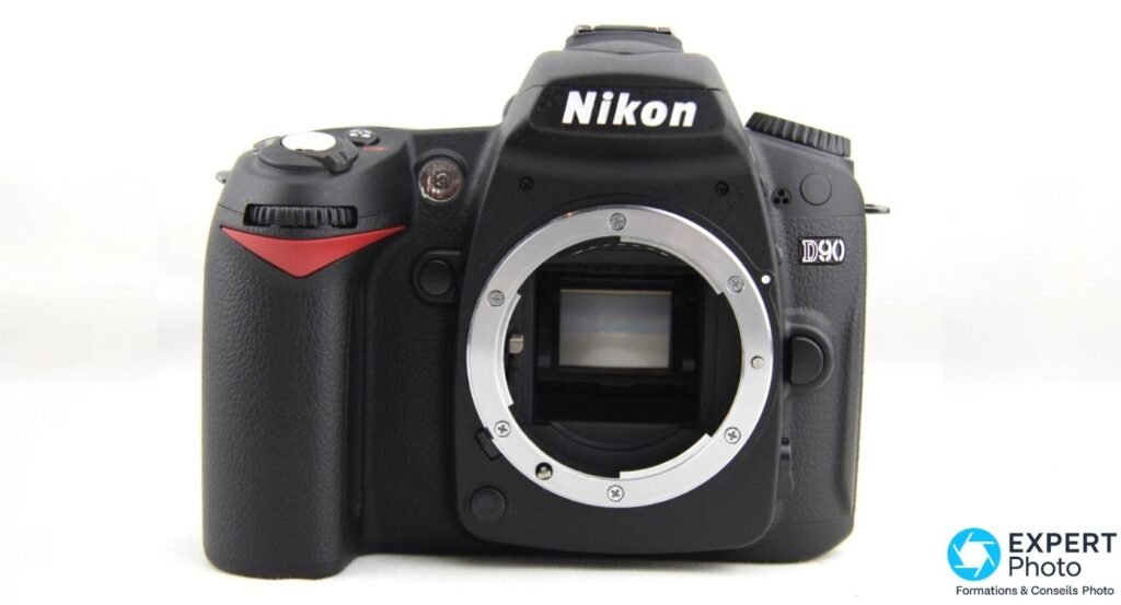 Boîtier nu Nikon D90 de face, monture Nikon F ouverte avec miroir et badge D90
