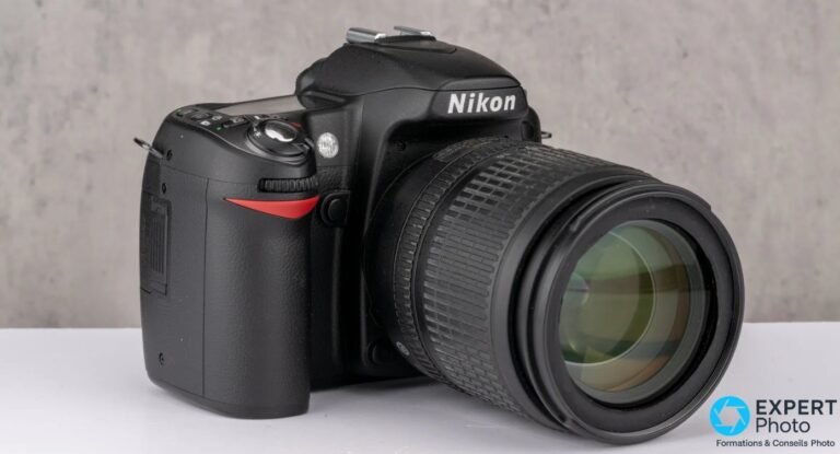 Nikon D90 avec objectif zoom Nikon VR, vu de trois quarts avant gauche sur fond gris