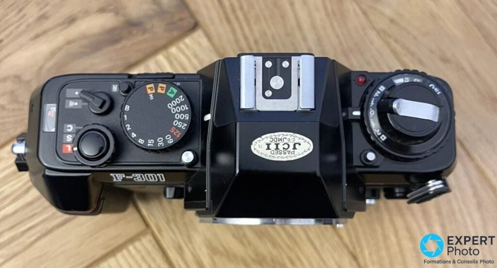 Nikon F-301 argentique vu de dessus : molette des vitesses, griffe flash et pastille JCII sur le prisme
