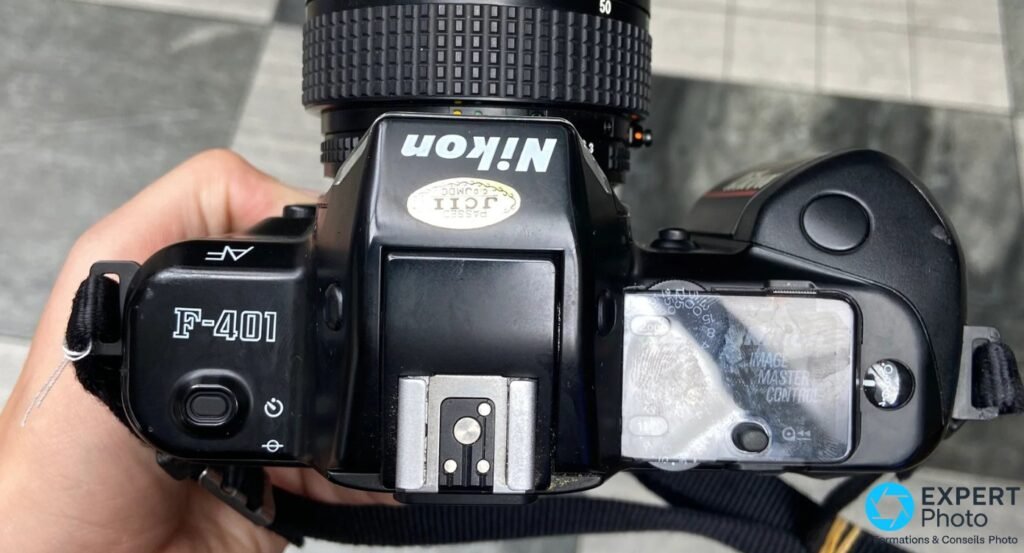 Vue de dessus du Nikon F-401, marquage AF F-401 lisible sur la coiffe gauche, griffe flash et sélecteur visibles. 