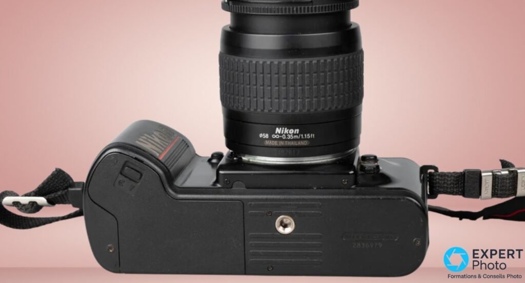Nikon F-401s vu de dessous, semelle avec prise de pied et numéro de série visibles, base objectif Nikon Nikkor.