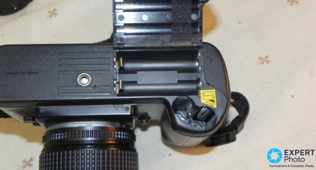 Compartiment à piles du Nikon F-401x ouvert, quatre logements pour piles AA, sticker d'orientation et filetage trépied.