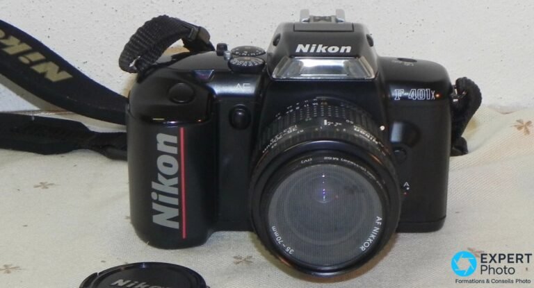 Nikon F-401x noir avec zoom AF Nikkor 35-70 mm monté et sangle Nikon, vue de face trois quarts sur tissu clair.