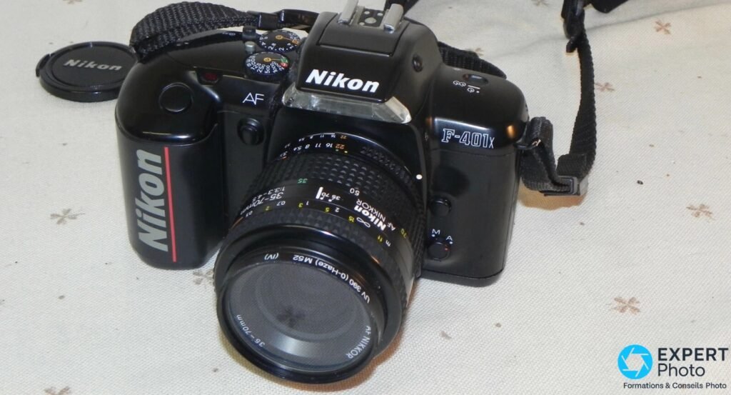 Nikon F-401x avec objectif AF Nikkor 35-70 mm et filtre UV, molette de modes et bouchon Nikon visibles.