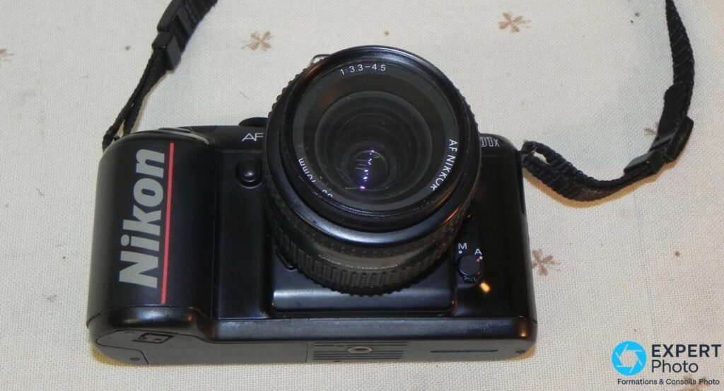 
Nikon F-401x vu en plongée, objectif AF Nikkor 35-70 mm 1:3.3-4.5, sélecteur M/A et sangle Nikon visibles.