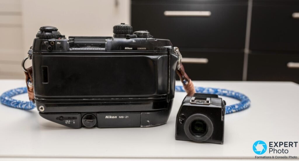 Nikon F4 de dos, poignée MB-21, avec son viseur prismatique amovible démonté et posé sur la table à droite