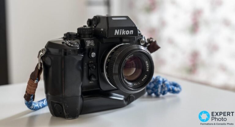 Reflex Nikon F4 noir de trois quarts avant gauche avec objectif Nikkor 50 mm, dragonne bleue, sur table blanche