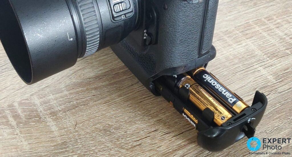  Compartiment piles ouvert sur la poignée verticale du Nikon F5, piles AA Panasonic Alkaline insérées, objectif visible 