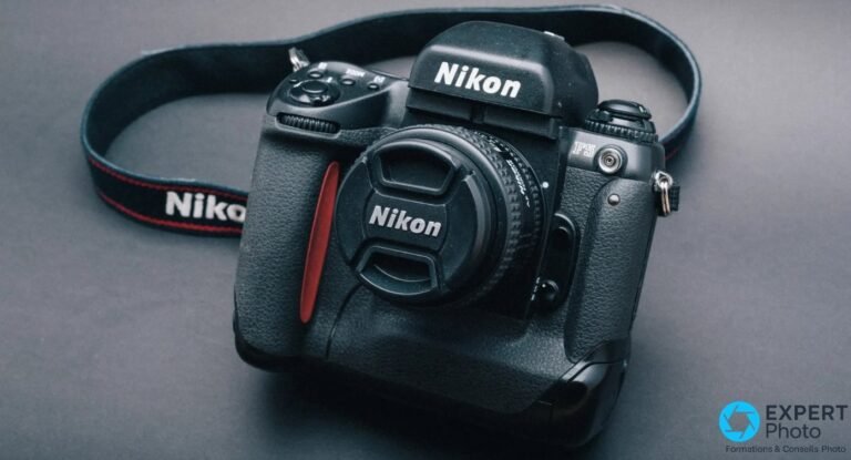 Nikon F5 vu de face trois quarts sur fond gris studio, objectif monté avec bouchon Nikon, sangle Nikon en arrière-plan