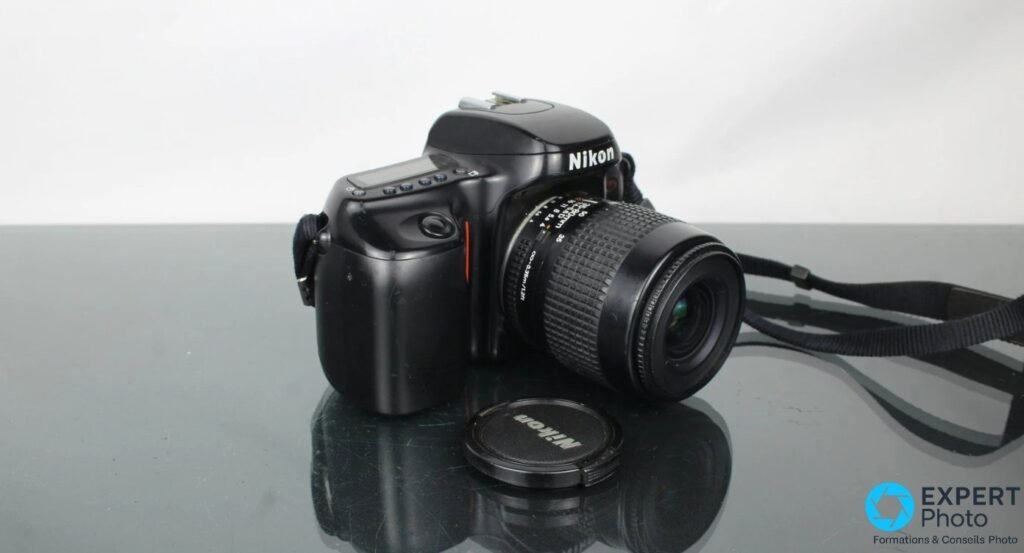 Nikon F50 de trois quarts, objectif AF Nikkor monte sur monture Nikon F, bouchon Nikon pose devant sur la table