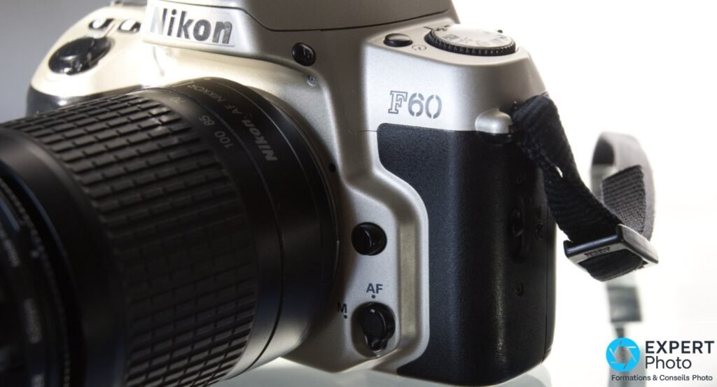 Nikon F60 vu de côté droit, inscription F60 en relief, commutateur AF/M, objectif zoom Nikon AF Nikkor monté, fond blanc