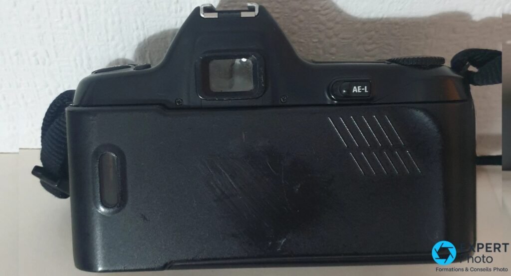 Vue arrière du Nikon F-601M dos fermé : viseur central, bouton AE-L à droite, zone striée de préhension et hublot à gauche