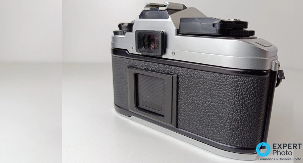 Nikon FG-20 vu de dos en angle 3/4 arrière, viseur oculaire et fenêtre mémo-film visibles, sans objectif