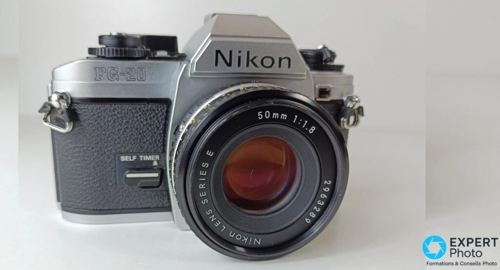 Nikon FG-20 vue 3/4 avant droit, objectif Nikon Lens Series E 50mm f/1.8, levier SELF TIMER visible côté gauche