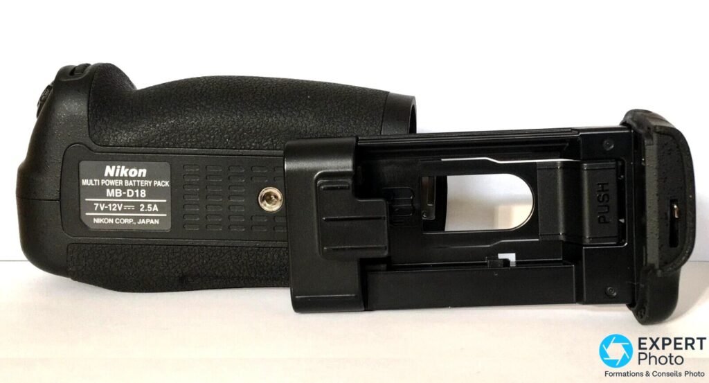  Grip Nikon MB-D18 en vue 3/4, plaque "Nikon Multi Power Battery Pack MB-D18" visible, compartiment batterie ouvert 