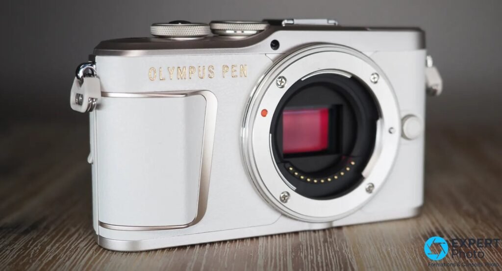 Olympus PEN E-PL10 blanc sans objectif, monture Micro 4/3 et capteur visibles, fond gris, vue 3/4 avant