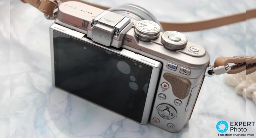 Olympus PEN E-PL8 vue arrière 3/4, écran LCD, molette PASM avec ART et SCN, griffe flash avec cache OLYMPUS