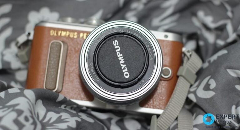 Olympus PEN E-PL8 brun de face, objectif M.Zuiko 14-42mm monté avec cache OLYMPUS, sangle grise, tissu fleuri