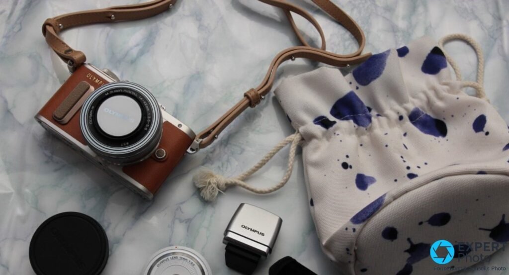 Flat lay Olympus PEN E-PL8 brun avec sangle cuir, pochette tissu blanche à pois, cache et accessoires OLYMPUS
