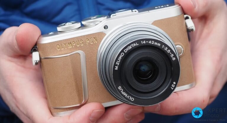 Olympus PEN E-PL9 coloris marron tenu à deux mains, vue de face avec objectif M.Zuiko 14-42mm monté.