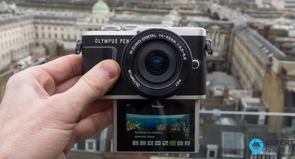 Olympus PEN E-PL9 noir tenu en main devant Londres, vue de face avec mode Panorama affiché à l'écran. 