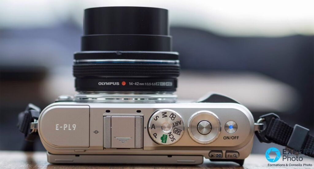Olympus PEN E-PL9 argenté vu de dessus, molette de modes et objectif M.Zuiko 14-42mm EZ rétracté.