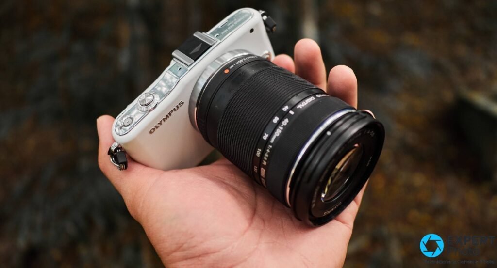  Olympus PEN E-PM1 blanc équipé d'un zoom Olympus M.Zuiko 40-150 mm tenu en main, fond extérieur flou 