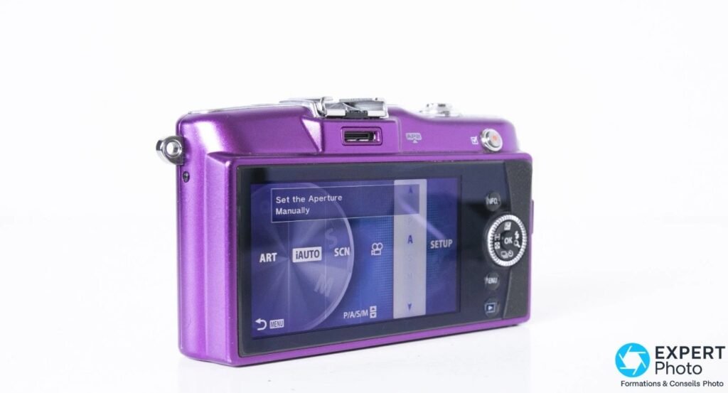 Olympus PEN E-PM1 vue arrière, écran LCD allumé affichant les modes ART, iAUTO, SCN, P/A/S/M et molette de navigation