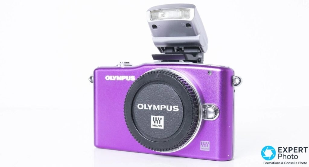 Olympus PEN E-PM1 violet vu de face, capuchon de monture monté et flash externe Olympus déplié sur la griffe accessoire