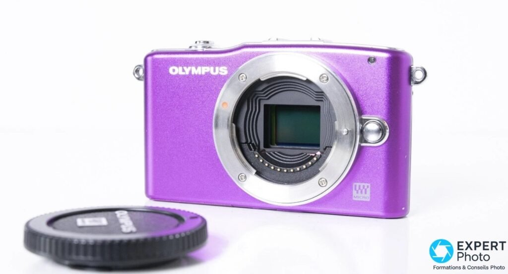 Olympus PEN E-PM1 violet en 3/4 avant, monture Micro Four Thirds ouverte, capteur visible et capuchon noir posé devant