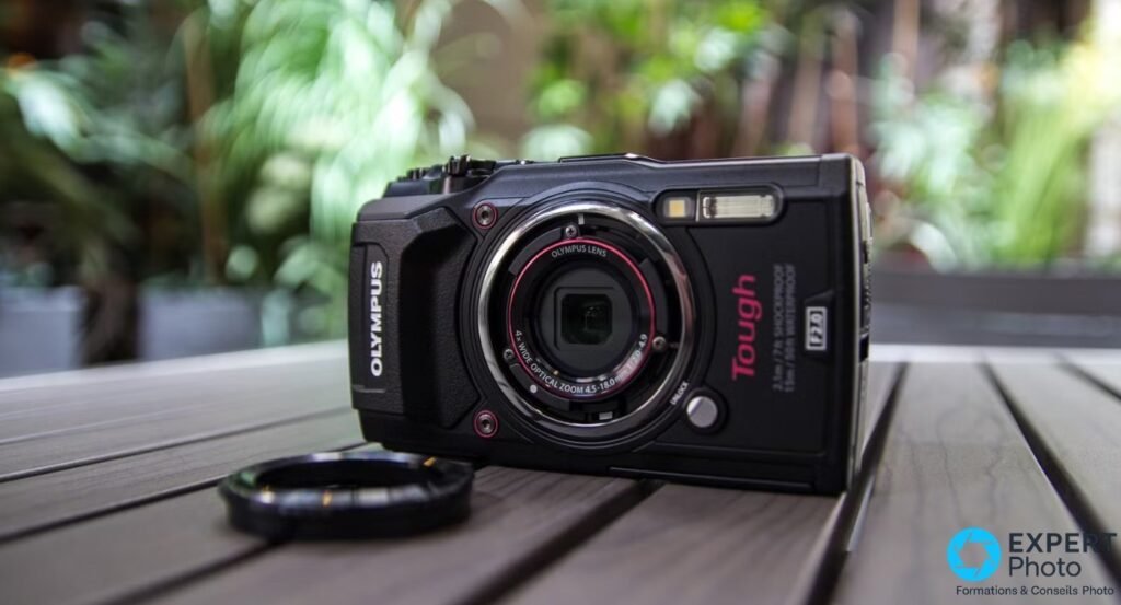 Olympus Tough TG-5 noir vu de face avec une bague de protection circulaire noire posée à côté sur la table en bois