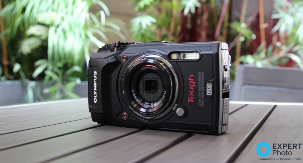 Olympus Tough TG-5 noir vu de face en 3/4 droite sur table en bois, objectif rétracté, logo OLYMPUS et Tough rouge visibles 