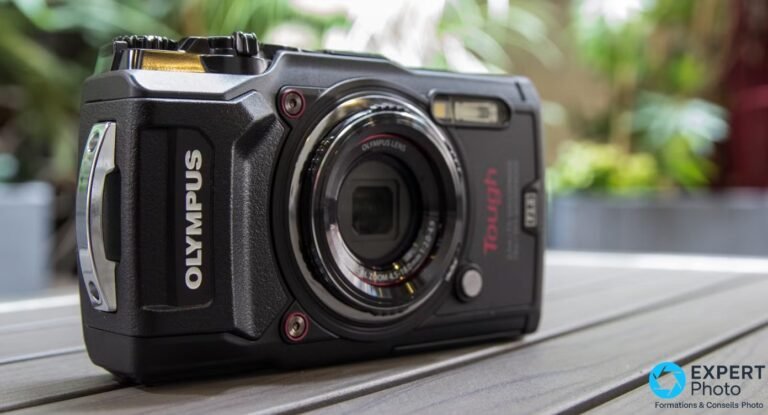 Olympus Tough TG-5 noir vu de face en 3/4 gauche, objectif rétracté, œillet de dragonne métallique visible sur le côté