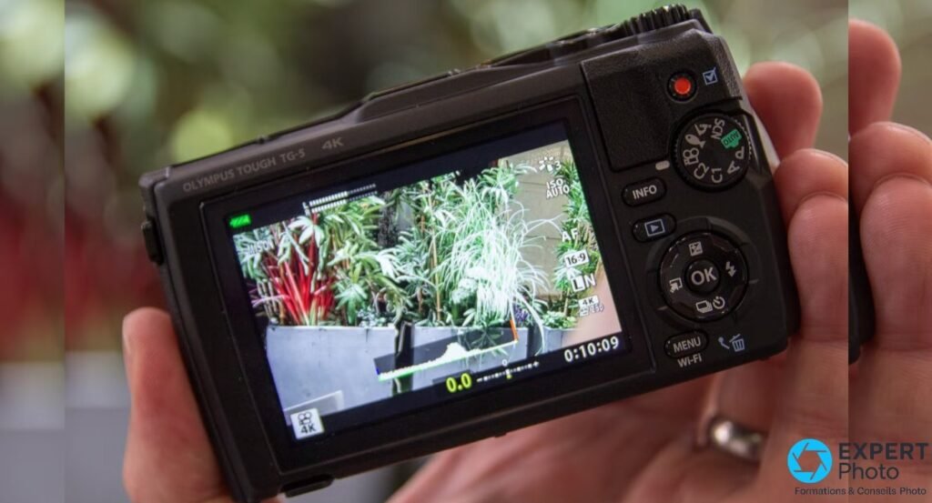 Olympus Tough TG-5 vu de dos tenu en main, écran arrière LCD allumé en mode vidéo 4K, molette de mode visible