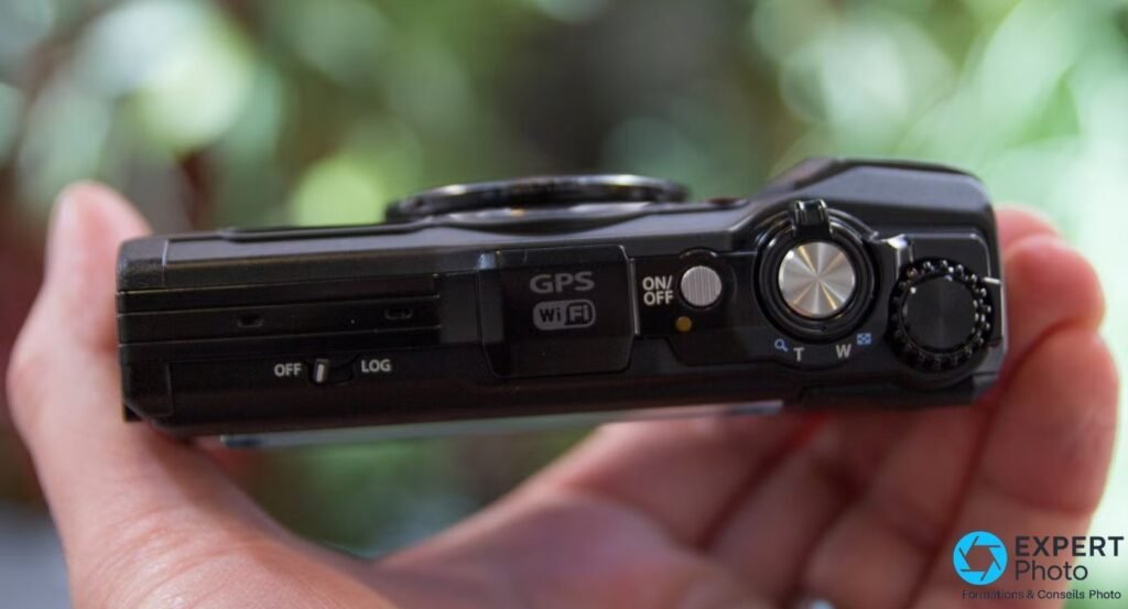 Olympus Tough TG-5 tenu en main vu de dessus, inscriptions GPS, Wi-Fi, ON/OFF, levier de zoom T/W et molette de mode
