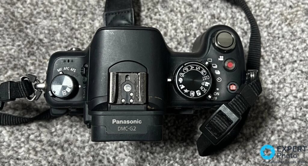 Dessus du Panasonic Lumix DMC-G2 avec sélecteur MF/AFC/AFS, molette de modes, griffe flash et étiquette DMC-G2.