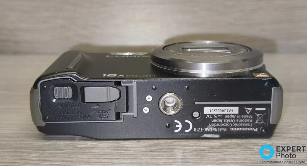 Panasonic DMC-TZ18 de dessous, trappe batterie et carte SD ouverte, étiquette modèle DMC-TZ18 et Made in Japan lisibles