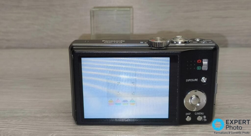 Panasonic DMC-TZ18 de dos, écran LCD allumé affichant une scène de cadrage, boutons Exposure et Q.Menu visibles à droite